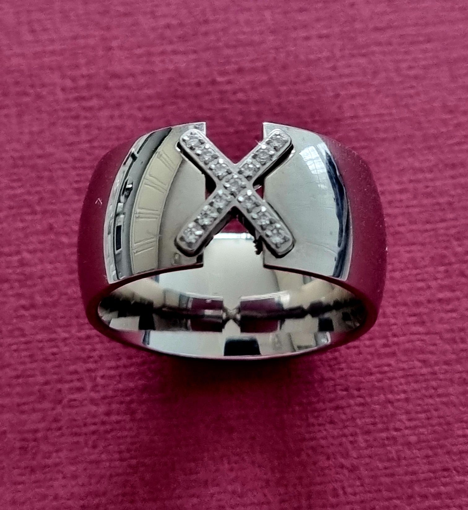 Anel grosso prateado, em aço, com um X em zirconias. T20
