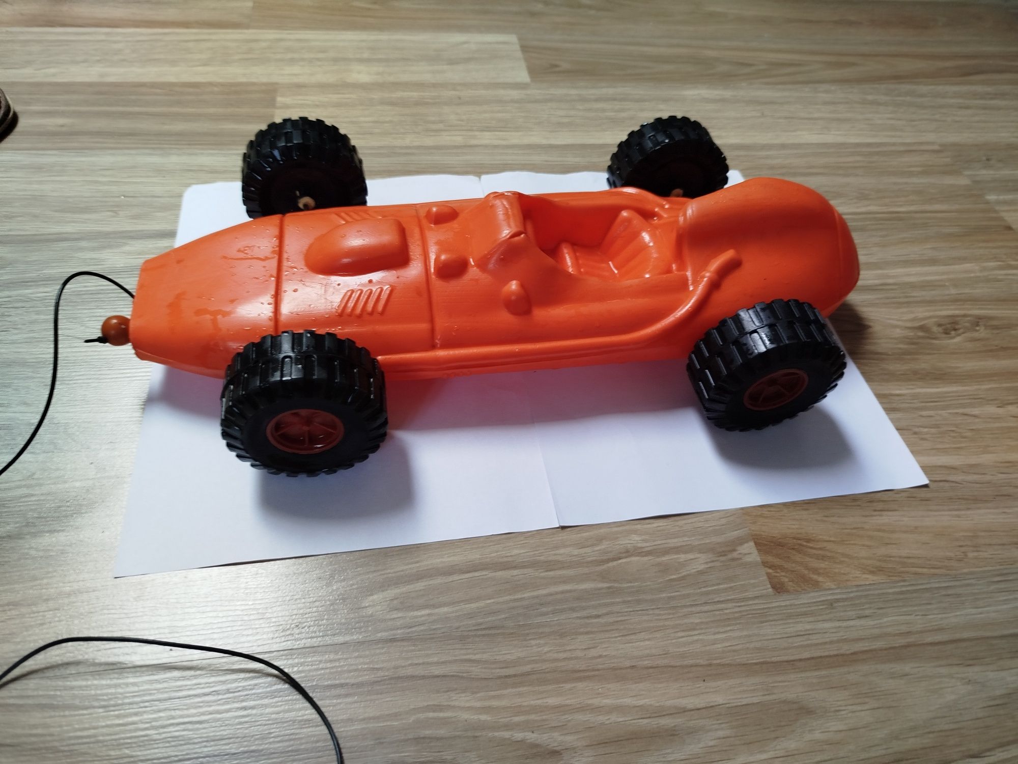 Plastikowe pomarańczowe autko, wyścigówka, z czarnymi dużymi kołami.