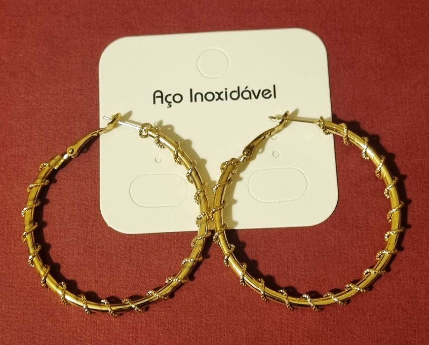 Brincos/argolas douradas, em aço, com cerca de 5cm de comprimento.