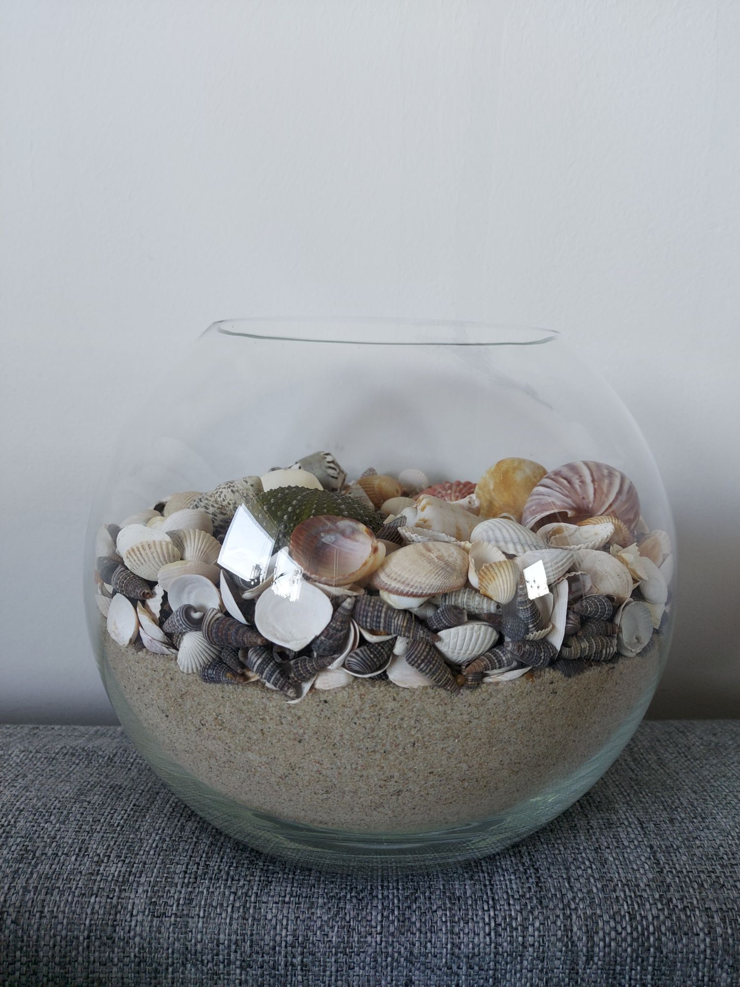 Dekoracja morska, muszelki muszle piasek w akwarium ze świeczka