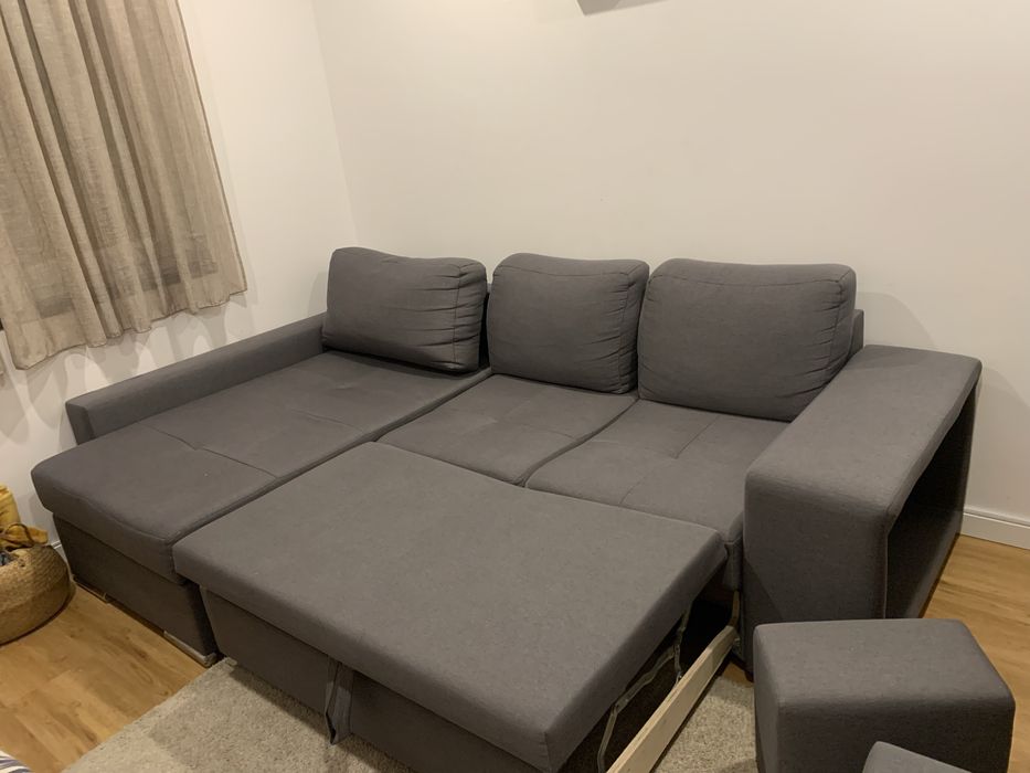 Sofa cama cinza com arrumaçao e dois bancos.