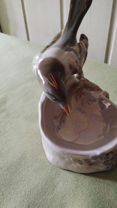 Porcelanowa figurka sroki na krawędzi podstawy.