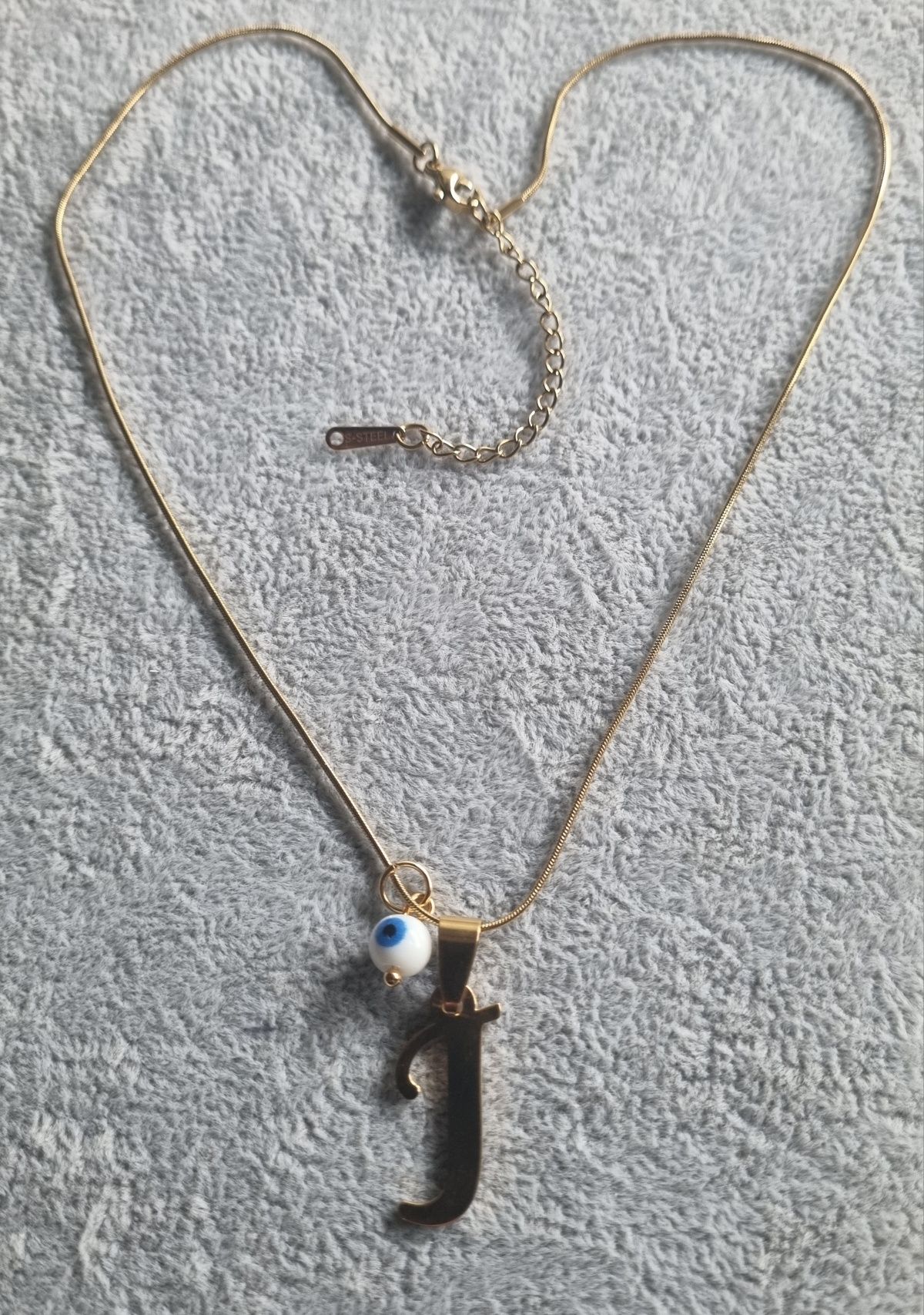 Colar dourado, em aço, com a letra "J" e olho turco. Tem extensor