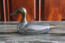Estatueta vintage de pato, corpo prateado e a cabeça e cauda douradas.
