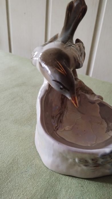 Porcelanowa figurka sroki na krawędzi podstawy.