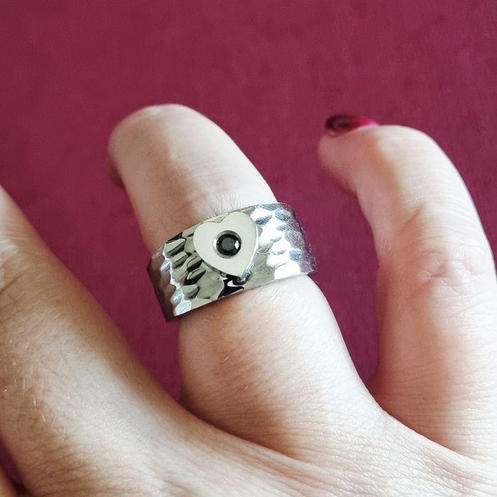 Anel prateado, em aço, com 1 coração com pedrinha preta no centro. T17