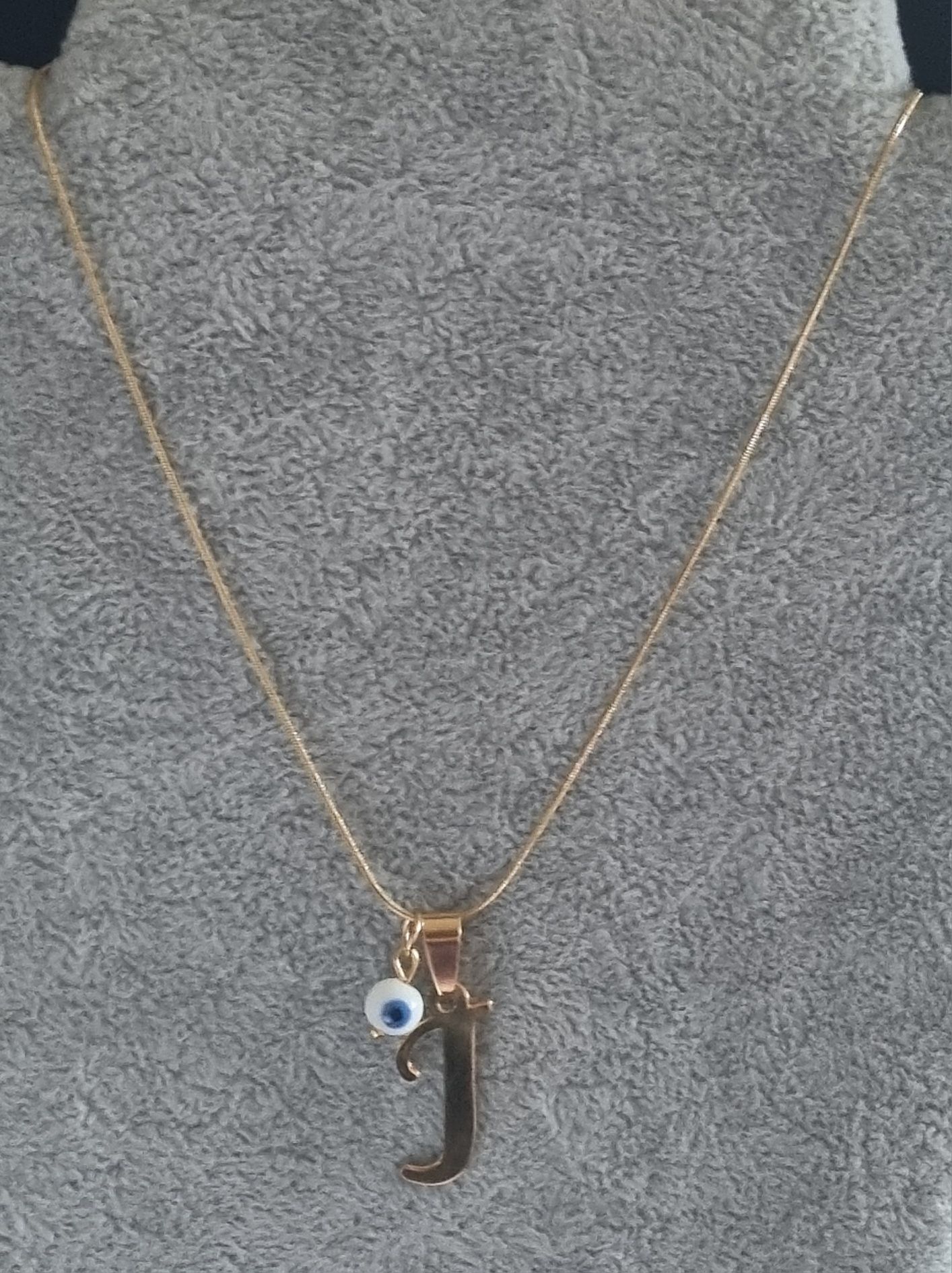 Colar dourado, em aço, com a letra "J" e olho turco. Tem extensor