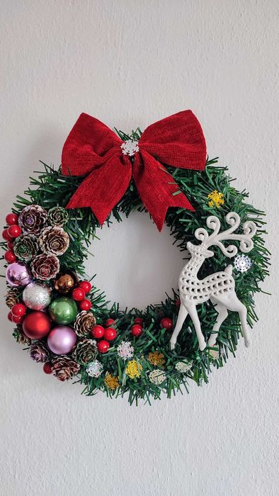 Wianek świąteczny na drzwi z czerwoną kokardą i białym reniferem