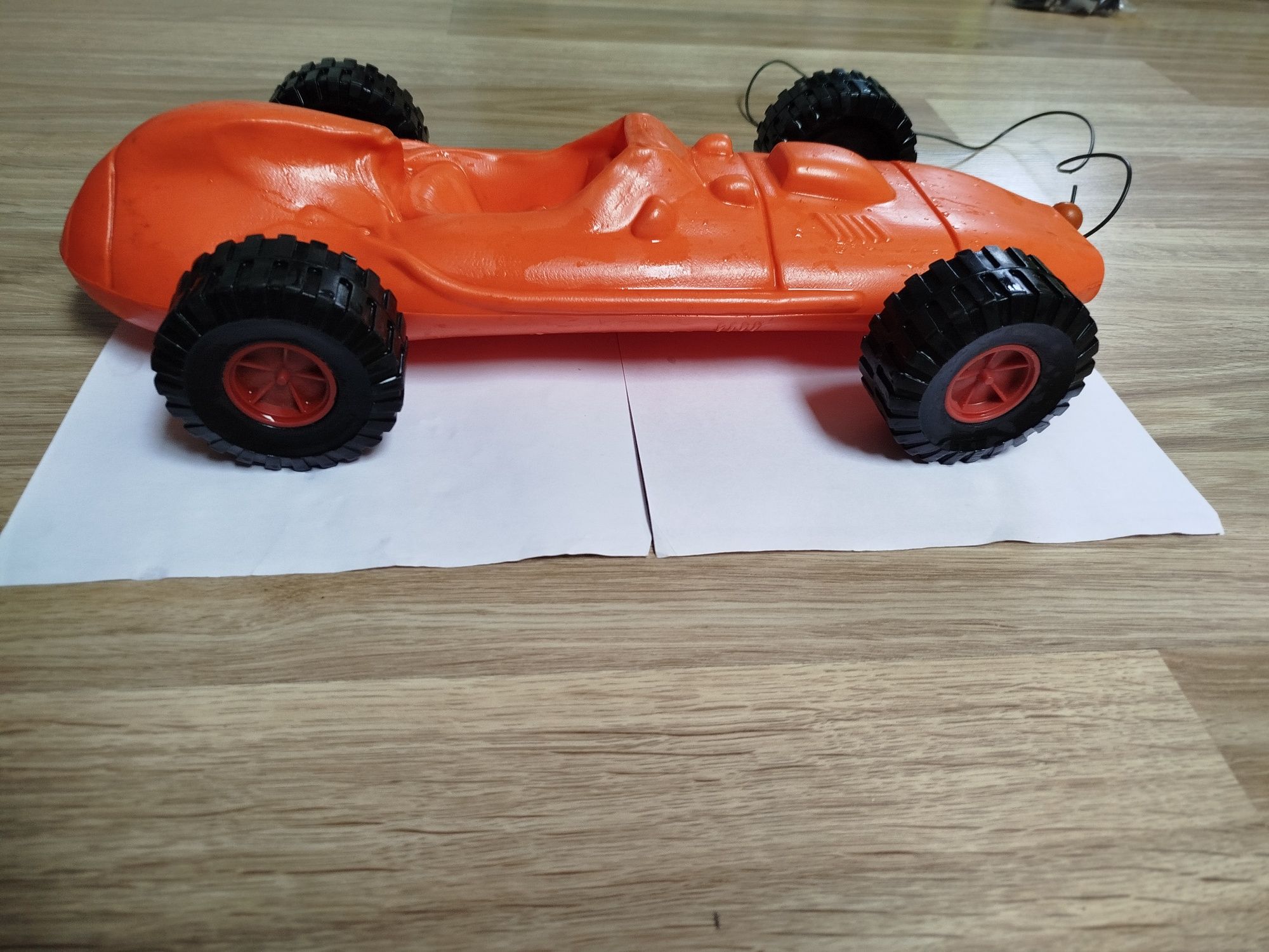 Plastikowe pomarańczowe autko, wyścigówka, z czarnymi dużymi kołami.