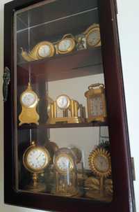 Vitrine de madeira com espelho atrás, contém 9 relógios em miniatura
