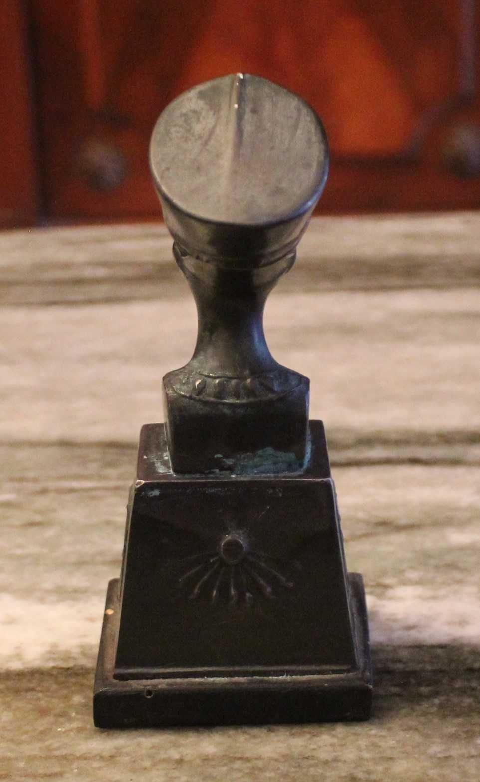 Busto de Nefertiti com 15,5cm de altura em metal sobre madeira.
