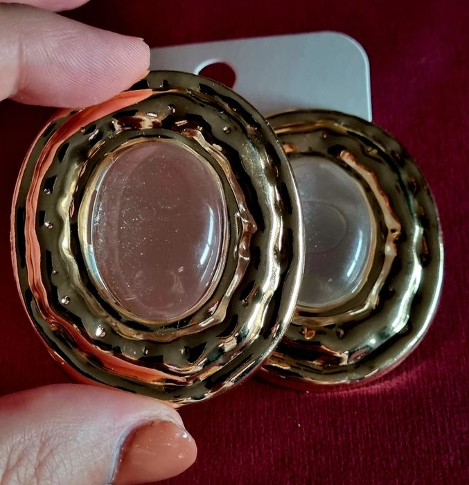 Brincos grandes dourados com acrílico oval transparente no centro.