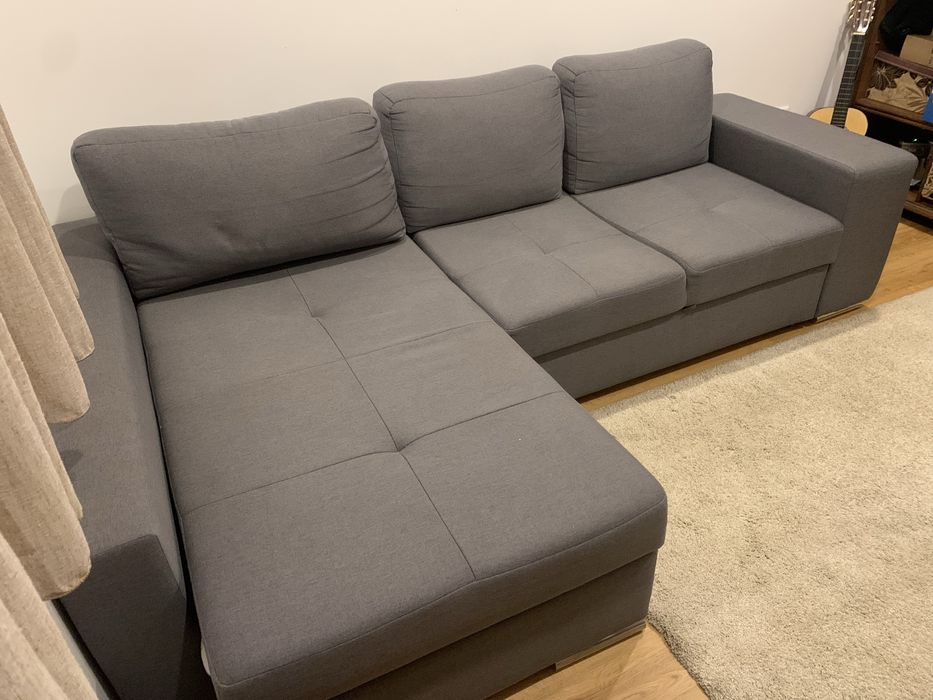 Sofa cama cinza com arrumaçao e dois bancos.