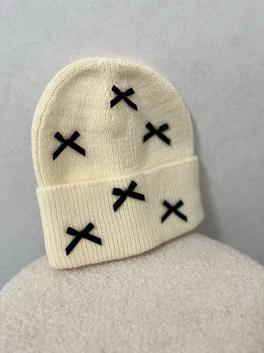 Зимня молочна в'язана шапка з чорними атласними бантами