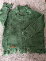 Zielony sweter zakończony postrzępieniami na ściągaczach
