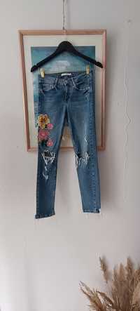 Skiny jeans z podarciami na kolanach i kwiatowym wzorem na prawym udzi