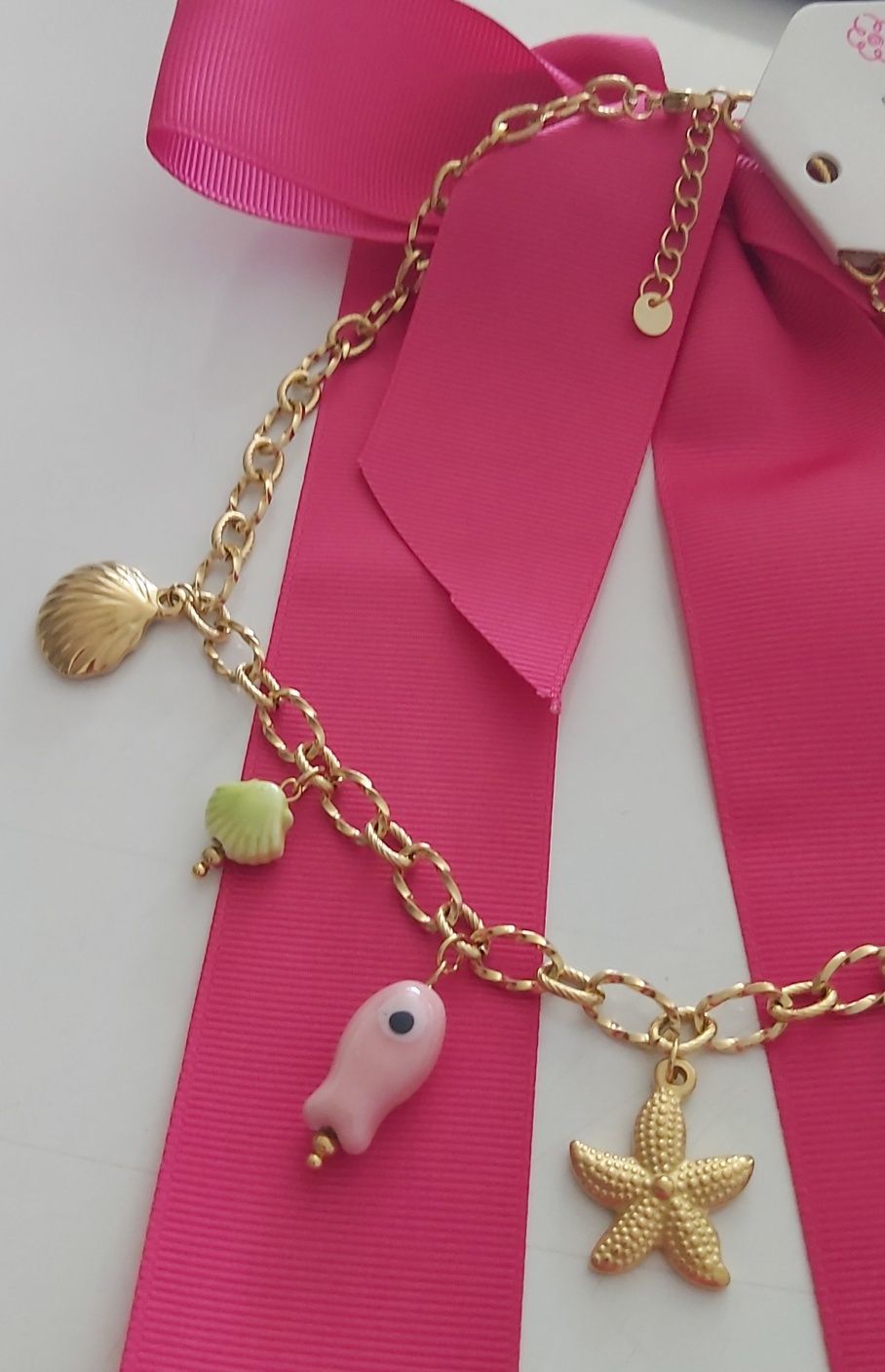 Colar dourado, em aço, com 7 pingentes diferentes. Tem extensor