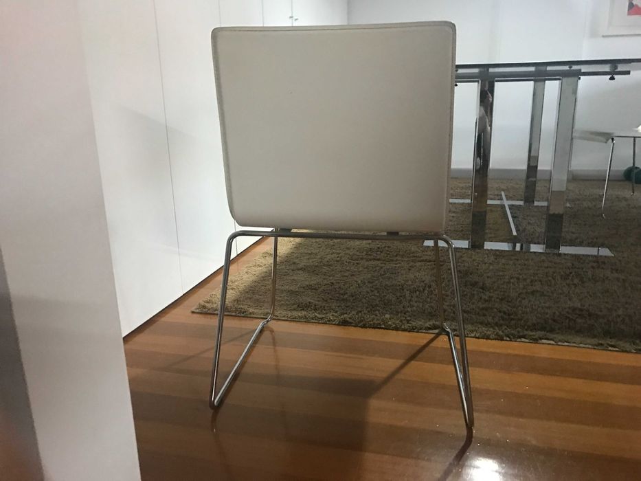 quatro cadeiras de pele branca e base em inox