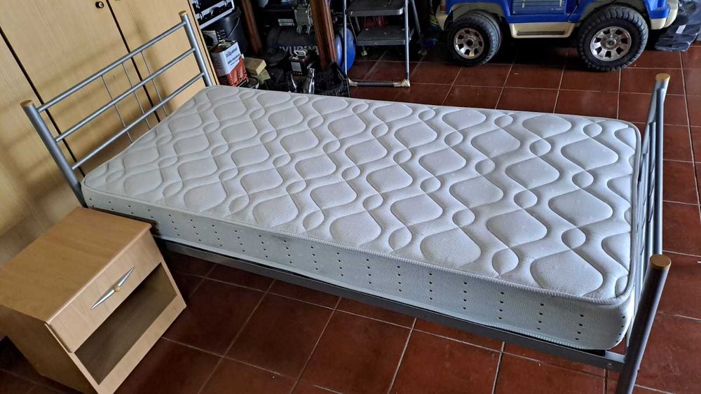 Cama individual com colchão e mesinha de cabeceira.