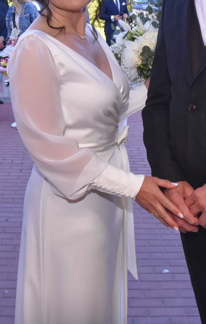 Minimalistyczna suknia ślubna z trenem i odpinanymi rękawami.