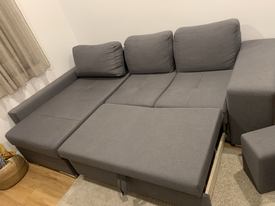 Sofa cama cinza com arrumaçao e dois bancos.