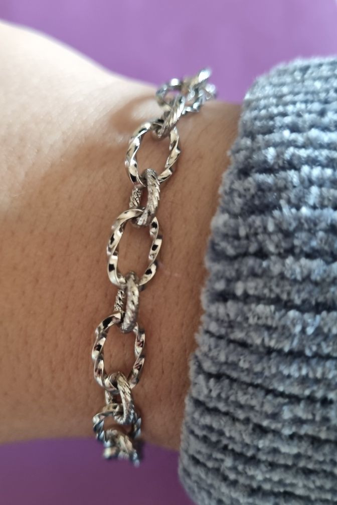 Pulseira prateada, em aço, com elos trabalhados. Tem extensor