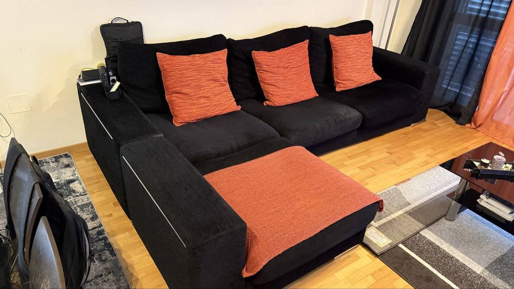 Sofá preto com chaise longue e 3 fronhas de almofada cor de laranja
