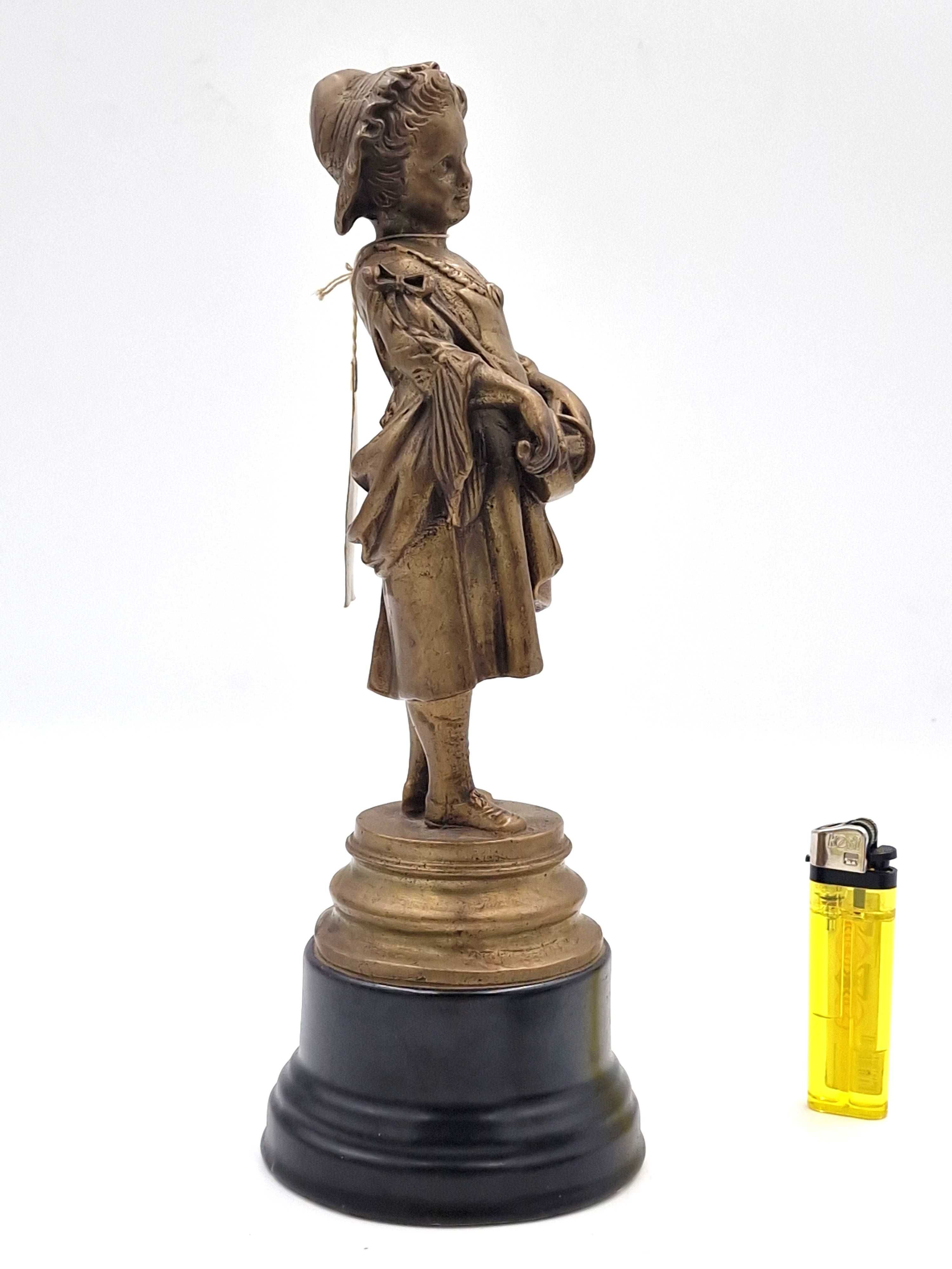 Rzeźba przedstawia dziewczynkę trzymającą w rękach