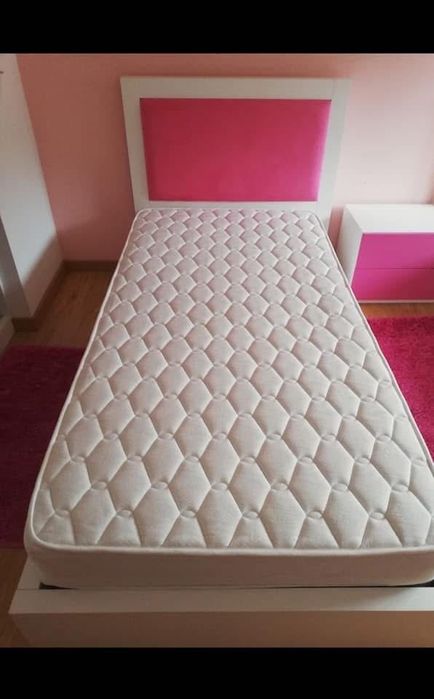Cama de solteira com mesinha de cabeceira com duas gavetas.