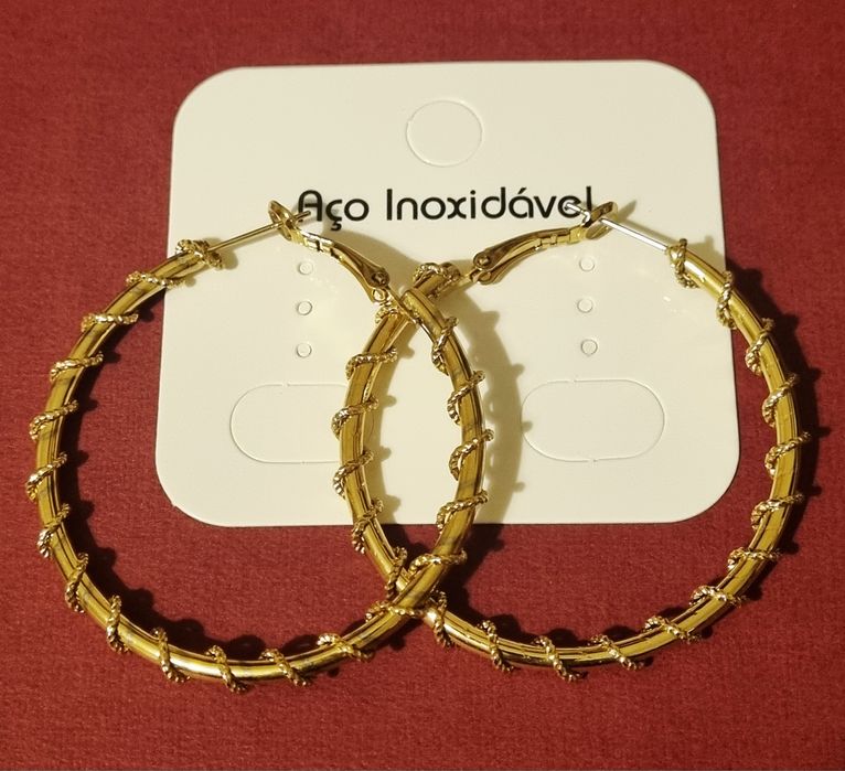 Brincos/argolas douradas, em aço, com cerca de 5cm de comprimento.