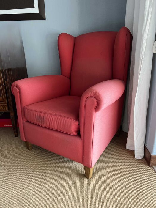 Cadeirão de orelhas forrado com tecido vermelho.