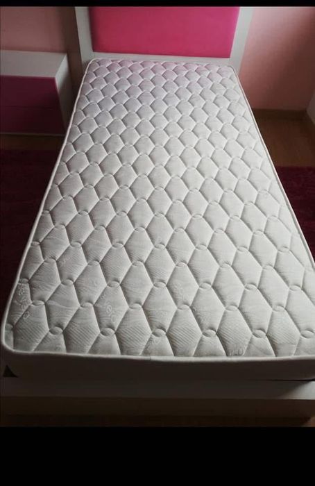 Cama de solteira com mesinha de cabeceira com duas gavetas.
