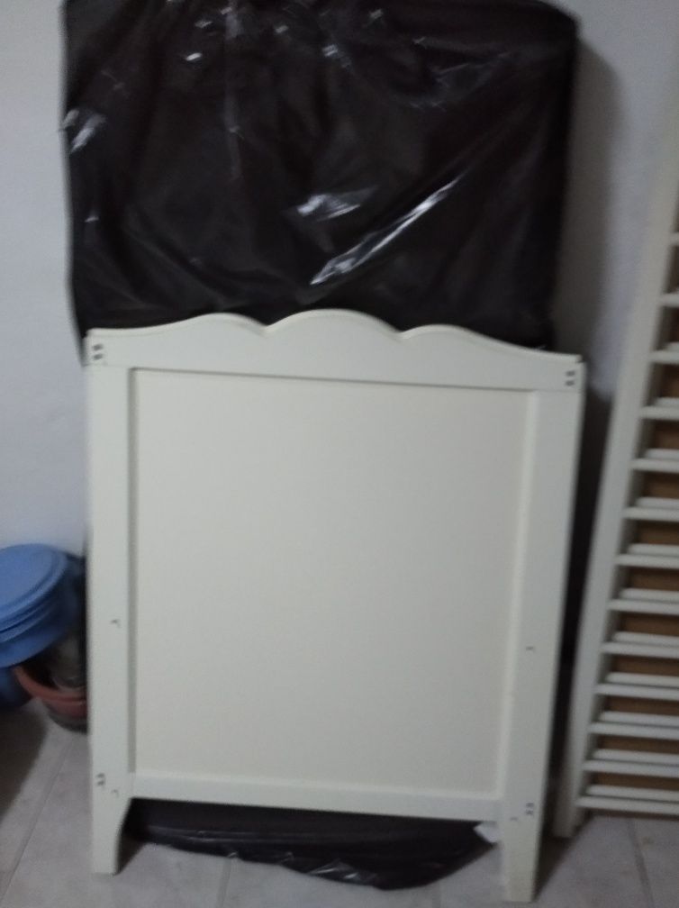 Cama de bebé branca de grades, com colchão.