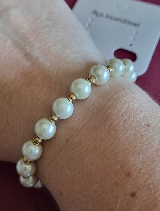 Pulseira dourada, em aço, com pérolas e fecho em T.