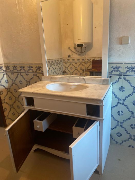 Móvle de casa de banho com tampo em mármore e espelho grande.