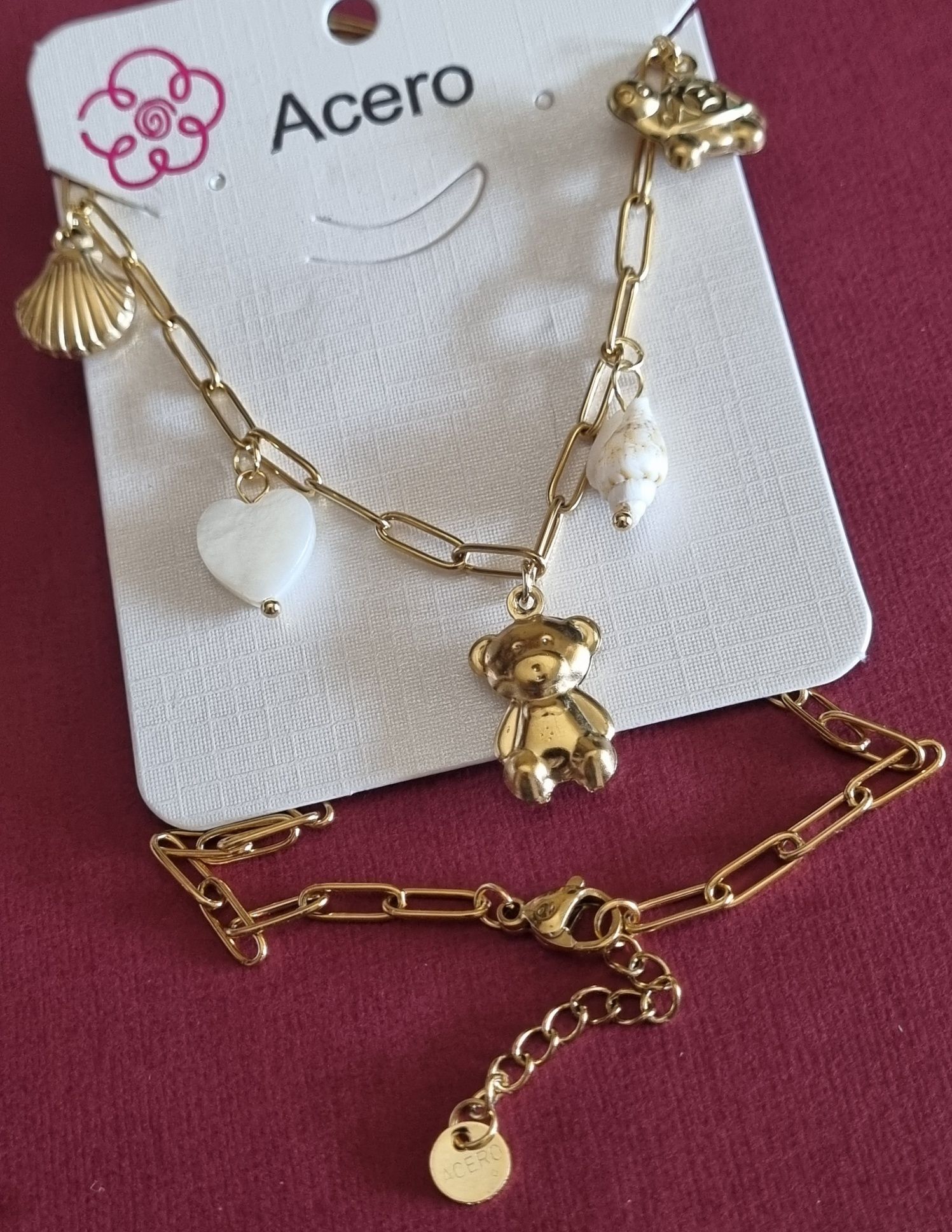Colar dourado, em aço, com 5 pingentes diferentes. Tem extensor