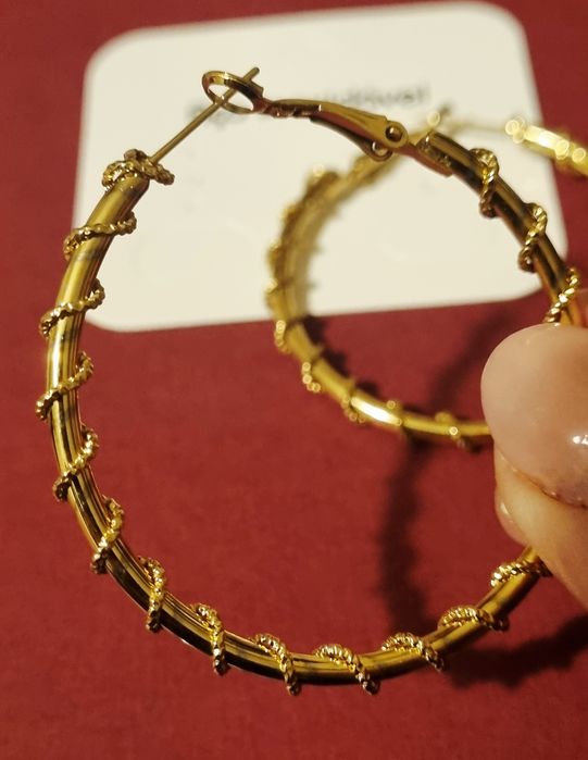 Brincos/argolas douradas, em aço, com cerca de 5cm de comprimento.