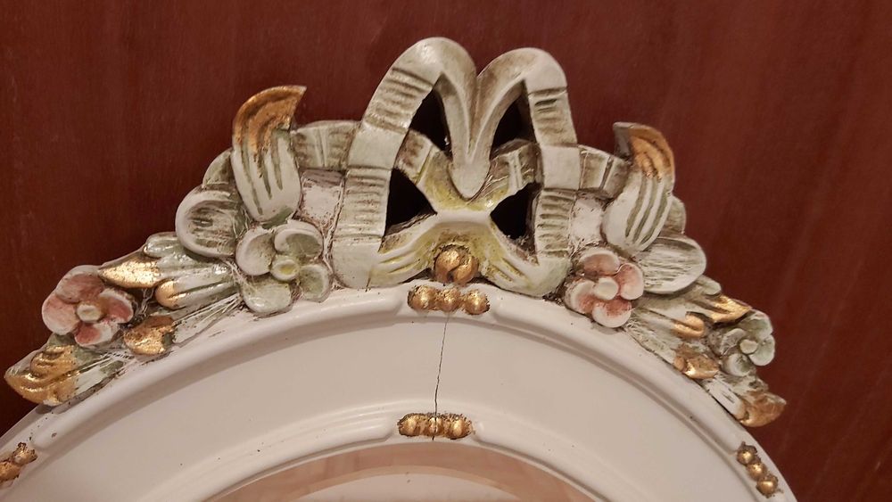 Espelho biselado com moldura de madeira com detalhes esculpidos.