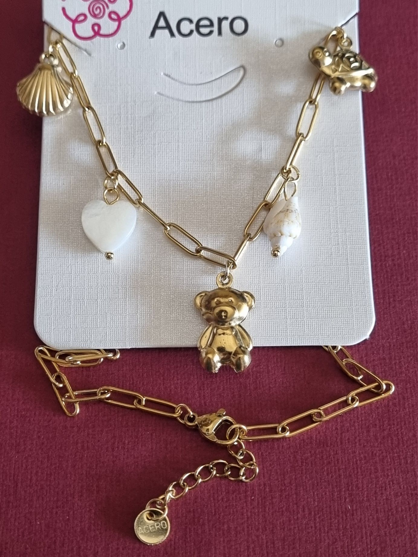 Colar dourado, em aço, com 5 pingentes diferentes. Tem extensor