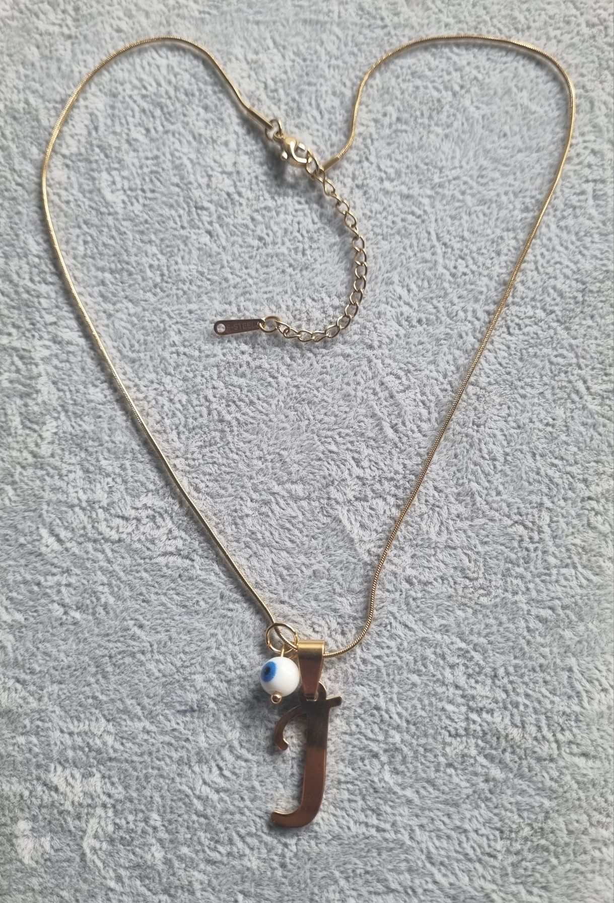 Colar dourado, em aço, com a letra "J" e olho turco. Tem extensor