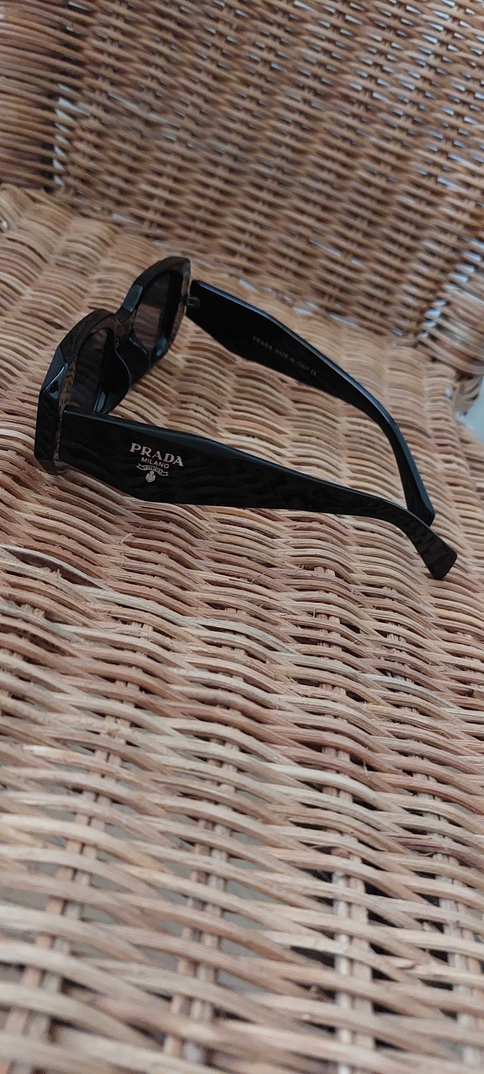 Óculos Prada preto com logótipo dourado.