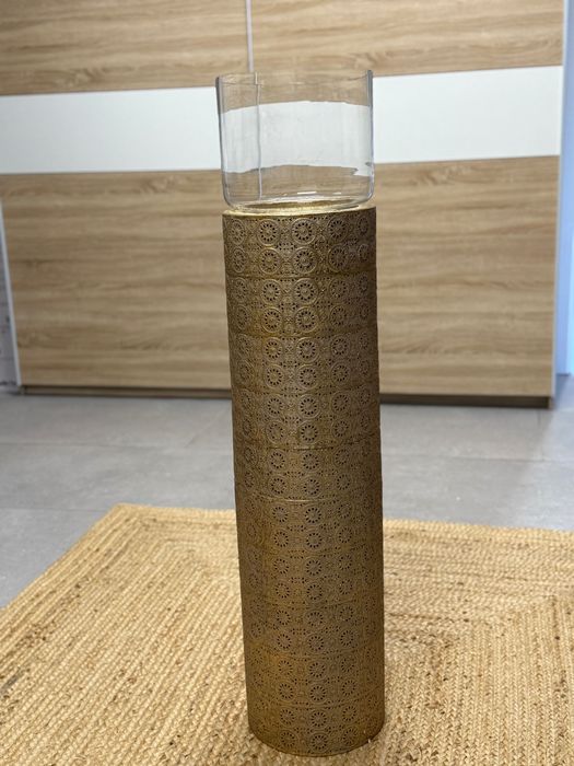 : Objeto decorativo cilíndrico dourado com suporte de vidro
