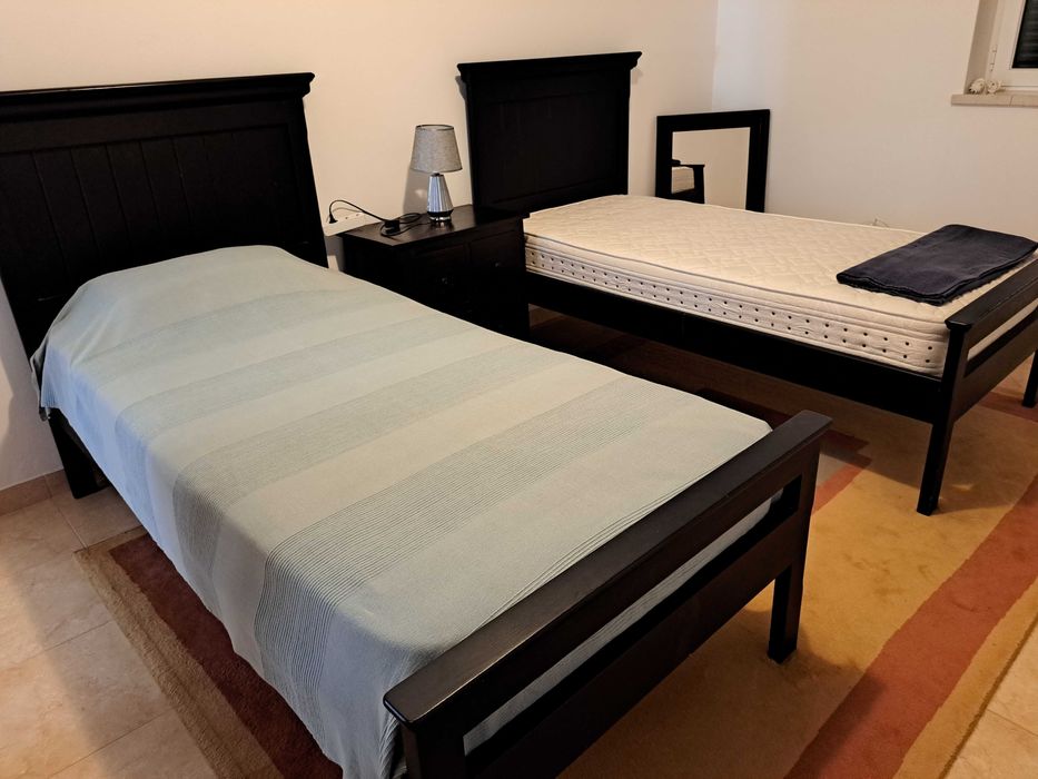2 camas de solteiro, com colchões, mesa de cabeceira.