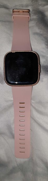 Zegarek Fitbit Versa 2 w kolorze różowego złota z różowym paskiem.