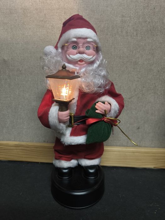 Pai Natal com candeeiro e saco de presentes com música.
Figura decorat