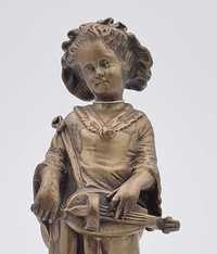 Rzeźba przedstawia dziewczynkę trzymającą w rękach