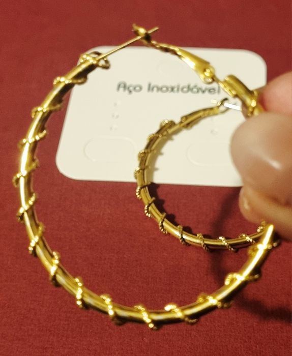 Brincos/argolas douradas, em aço, com cerca de 5cm de comprimento.