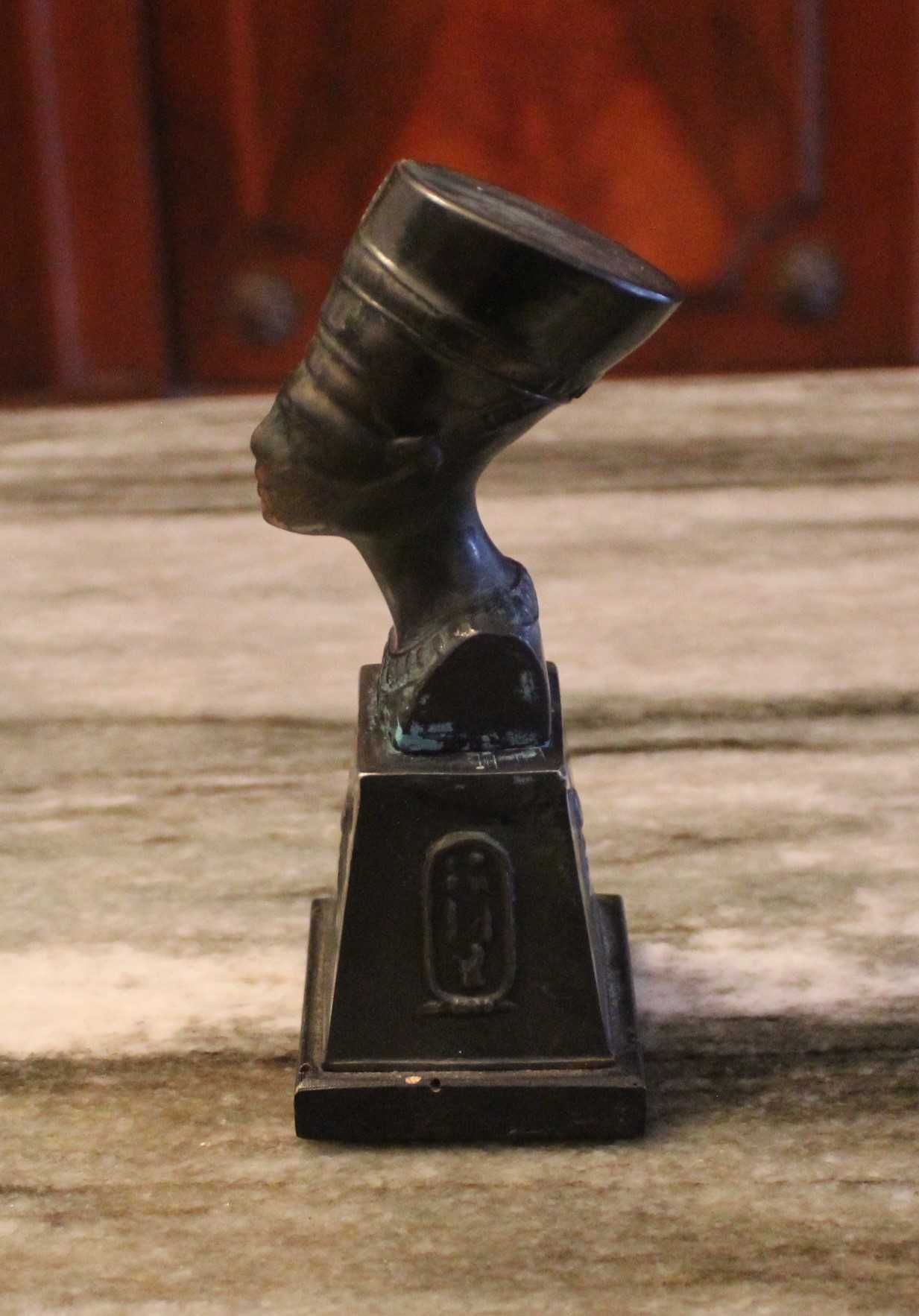 Busto de Nefertiti com 15,5cm de altura em metal sobre madeira.
