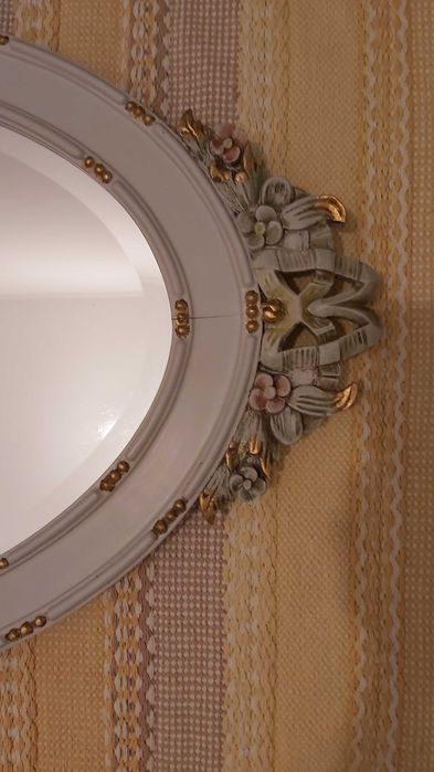 Espelho biselado com moldura de madeira com detalhes esculpidos.