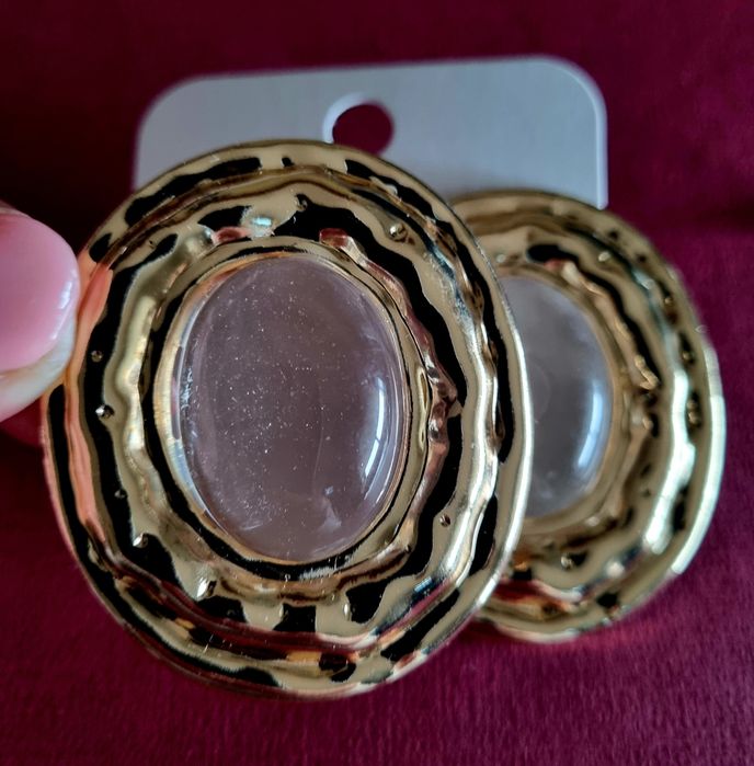 Brincos grandes dourados com acrílico oval transparente no centro.